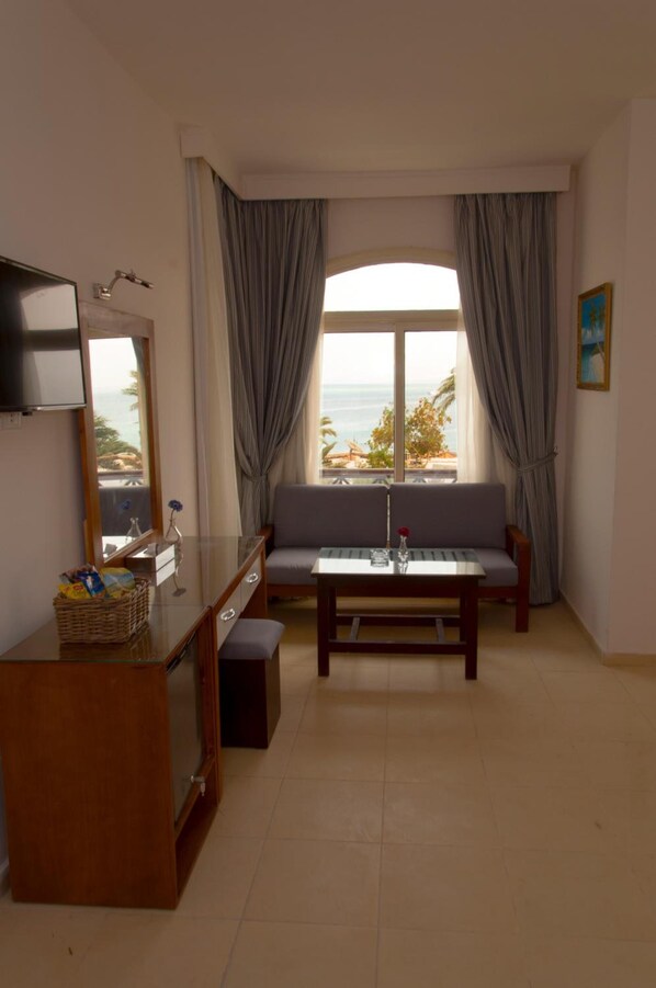 Una habitación con sofá, una mesita, televisor y ventana con cortinas.