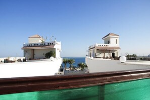 A rooftop terrace with a clear view of the sea, featuring two white buildings with tiled roofs and a wooden railing in the foreground. - Elaria (Hurghada)