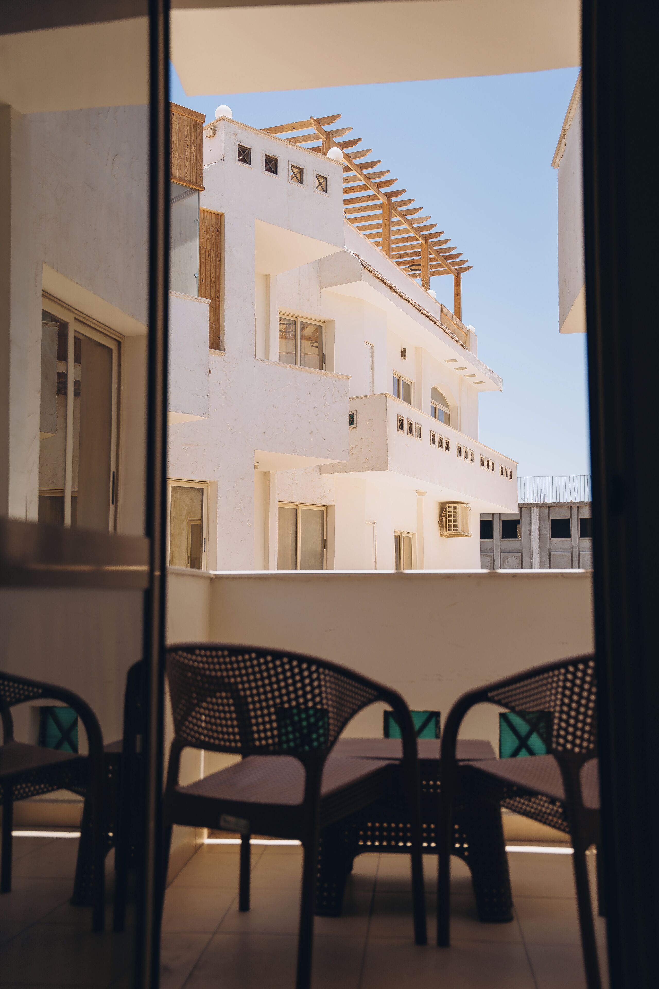 Un balcon avec des fauteuils en osier, un bâtiment blanc doté de nombreuses fenêtres et de balcons, et un ciel dégagé.