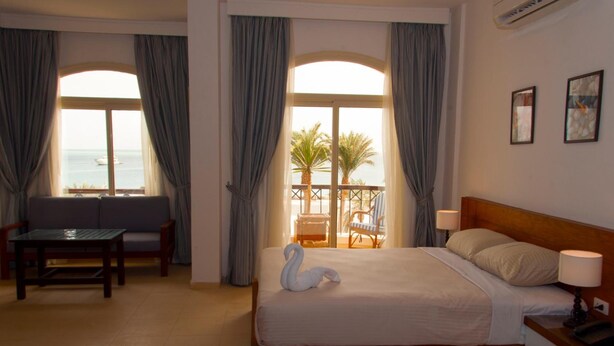 A hotel room with a bed, a small table, a chair, and a balcony with a view of the sea. -  Fantasia Hotel (Hurghada)
