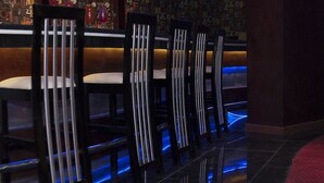 A row of bar-style chairs with vertical light strips, a bar counter, and a patterned wall in the background. -  Fantasia Hotel (Hurghada)