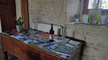 A wooden table with magazines and a bottle, a potted plant, and a window with a cactus.