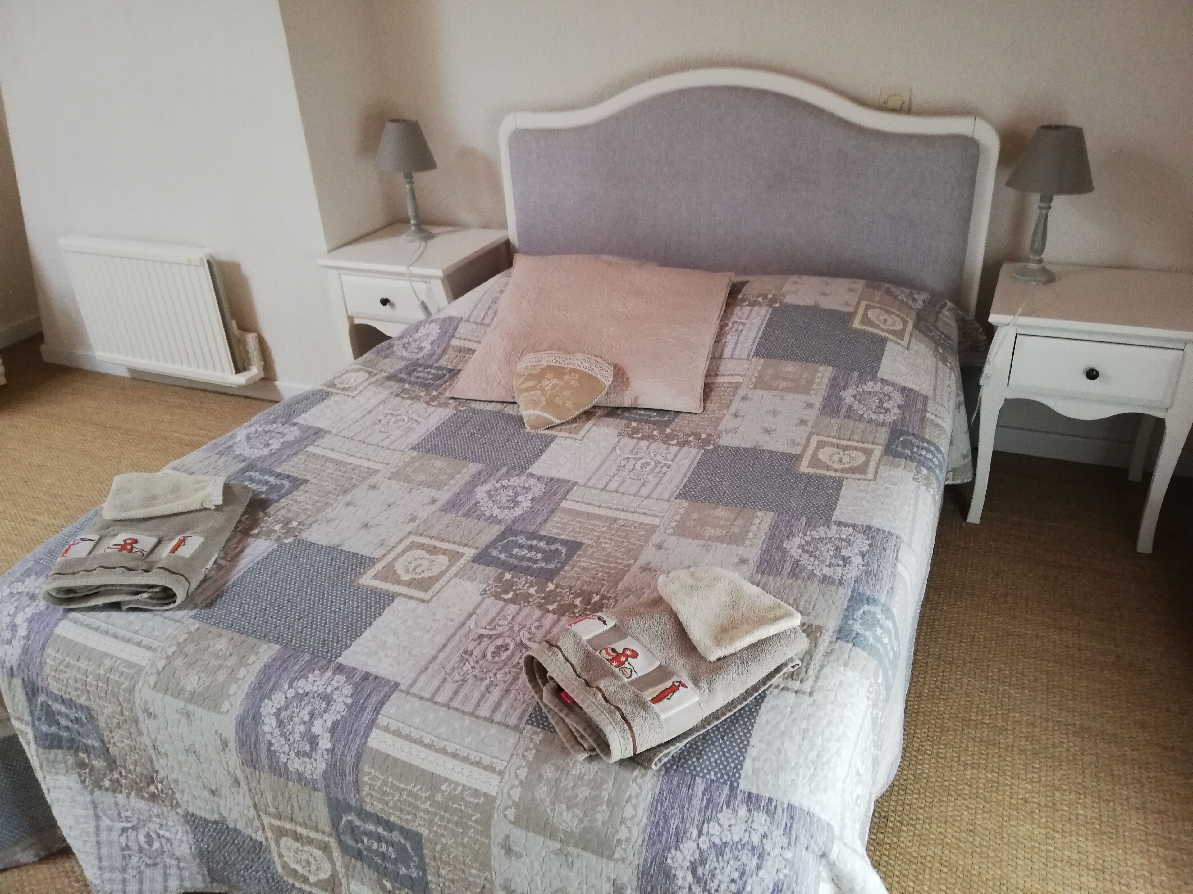 A neatly made bed with a patchwork quilt, two bedside tables with lamps, and a radiator in the background.