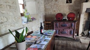 A rustic room with a wooden table covered in brochures, a potted plant, and a vintage dresser with two red objects on top. - Les Chenêts (Chenay)