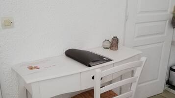 Een wit bureau met een laptop, een notitieboek en een pen. Er staat een kleine vaas met bloemen en er hangt een foto aan de muur.