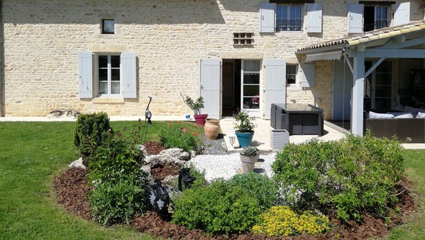 A stone building with a garden in front, featuring a variety of plants and a small pond. - Les Chenêts (Chenay)