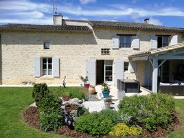 Un bâtiment en pierre avec un jardin à l’avant, agrémenté de diverses plantes et d’un petit étang.