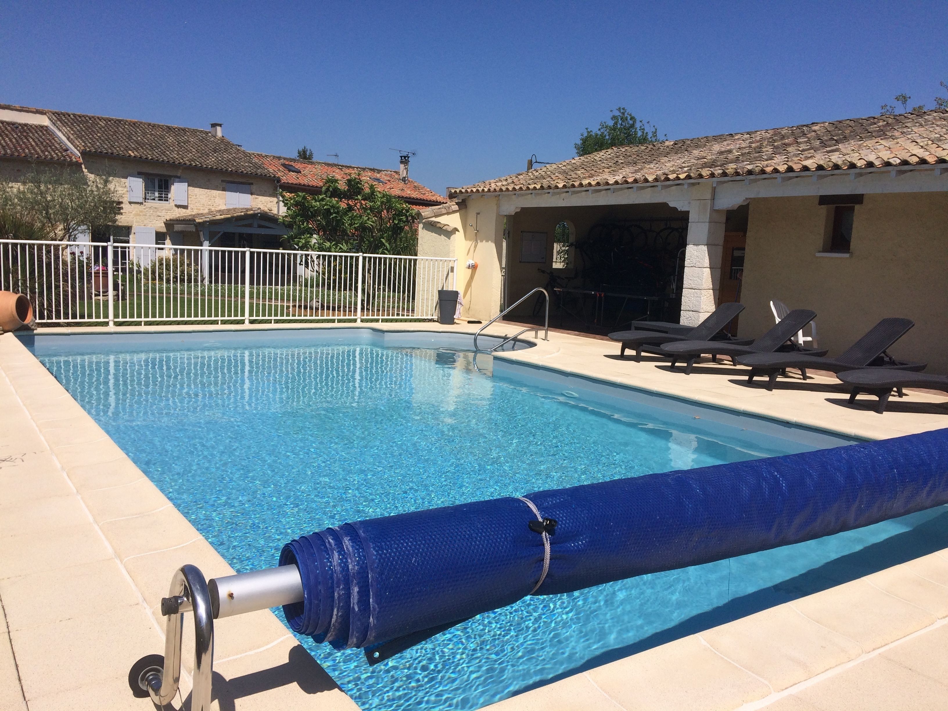Ein Swimmingpool mit blauer Abdeckung, Liegestühlen und einem weißen Zaun.
