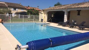 Ein Swimmingpool mit blauer Abdeckung, Liegestühlen und einem weißen Zaun.
