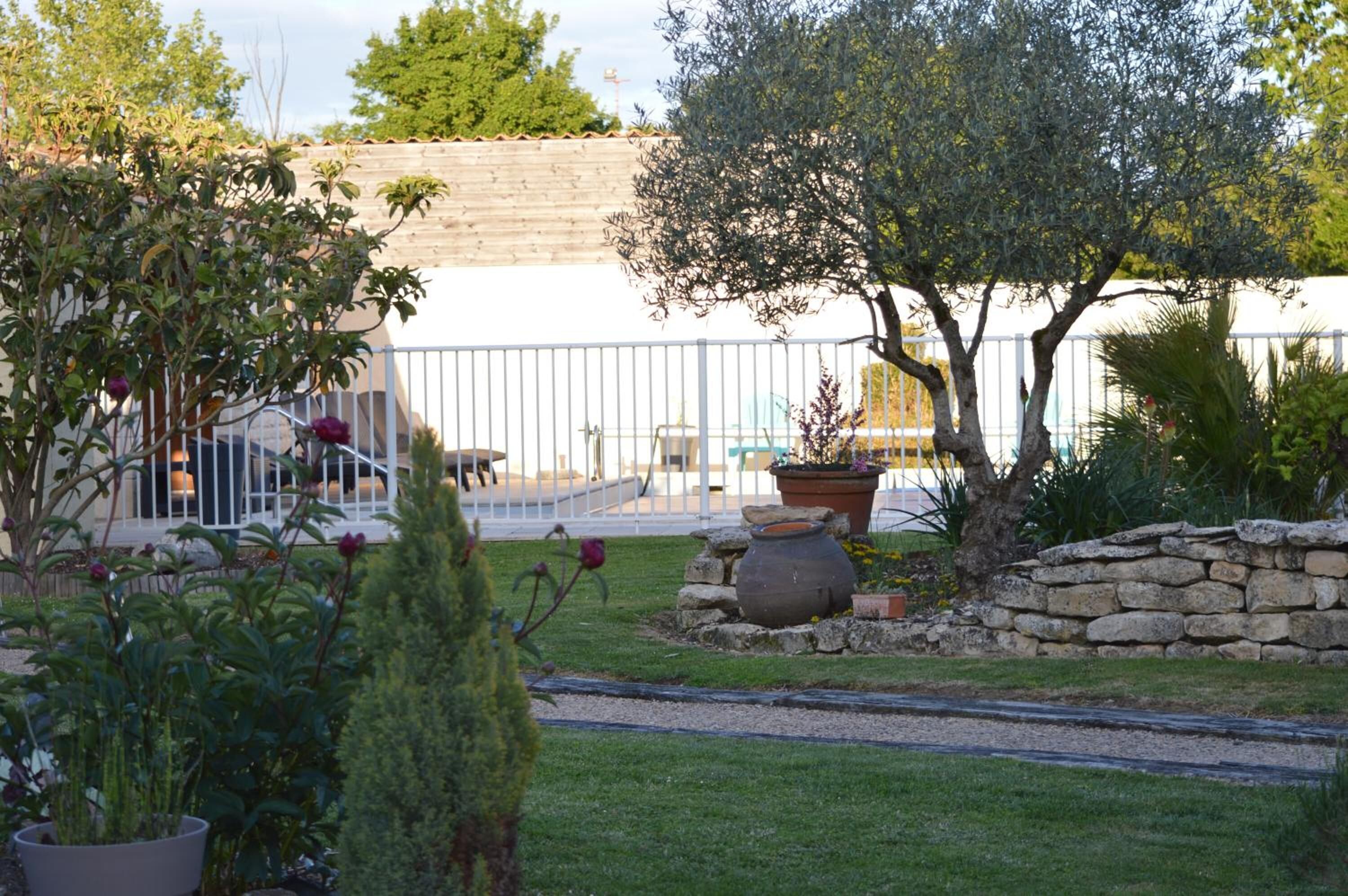A garden with a stone wall, potted plants, and a metal fence.
