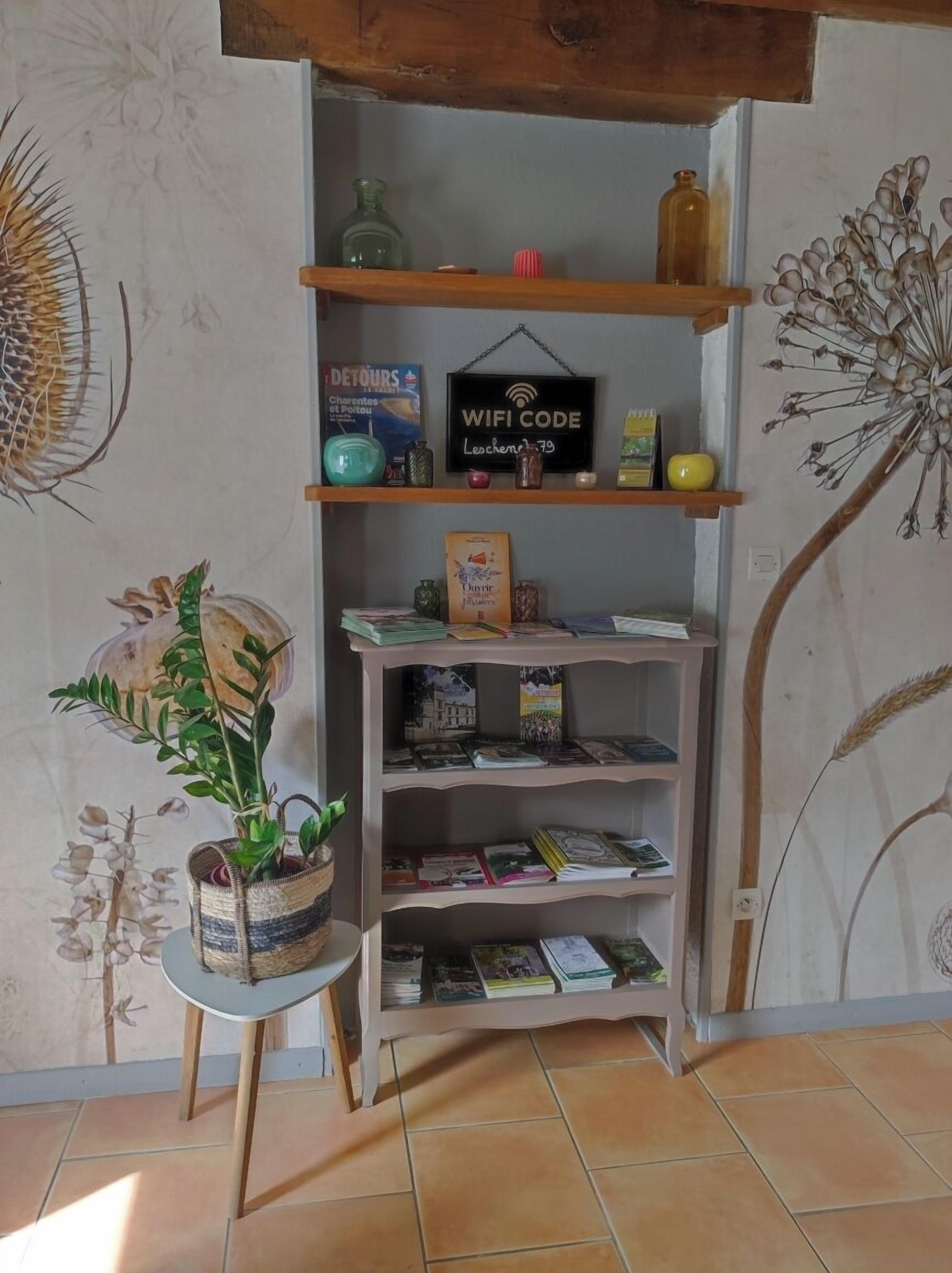Una habitación con una estantería de madera que contiene libros, objetos decorativos y un cartel con el código WiFi.