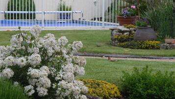 Jardí amb tanca blanca, diverses plantes i zona de piscina al fons.