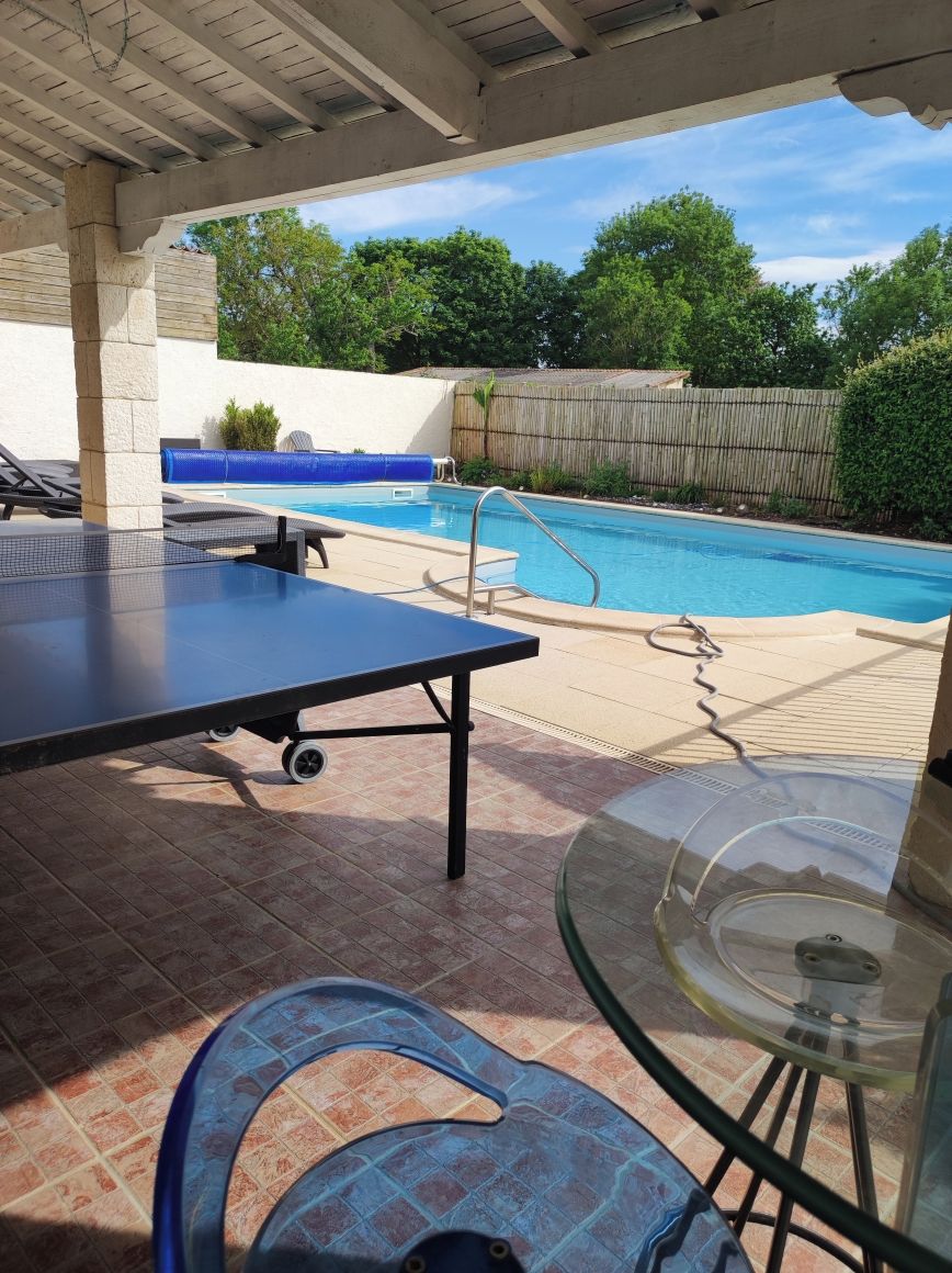 An outdoor pool area with a table and chairs, a covered patio, and a view of the pool.
