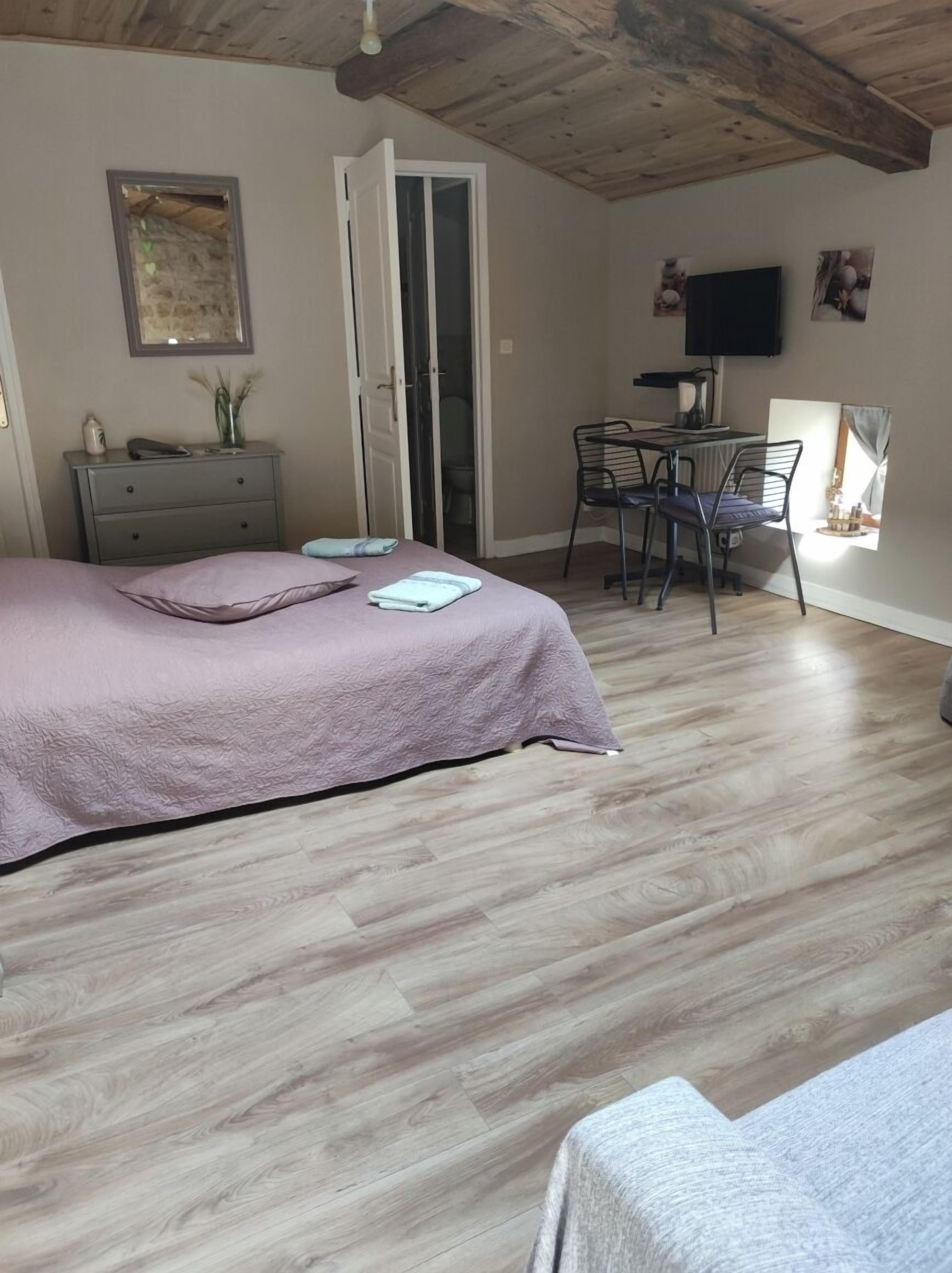 A bedroom with a bed, a dresser, a desk with a chair, a television, and a window.
