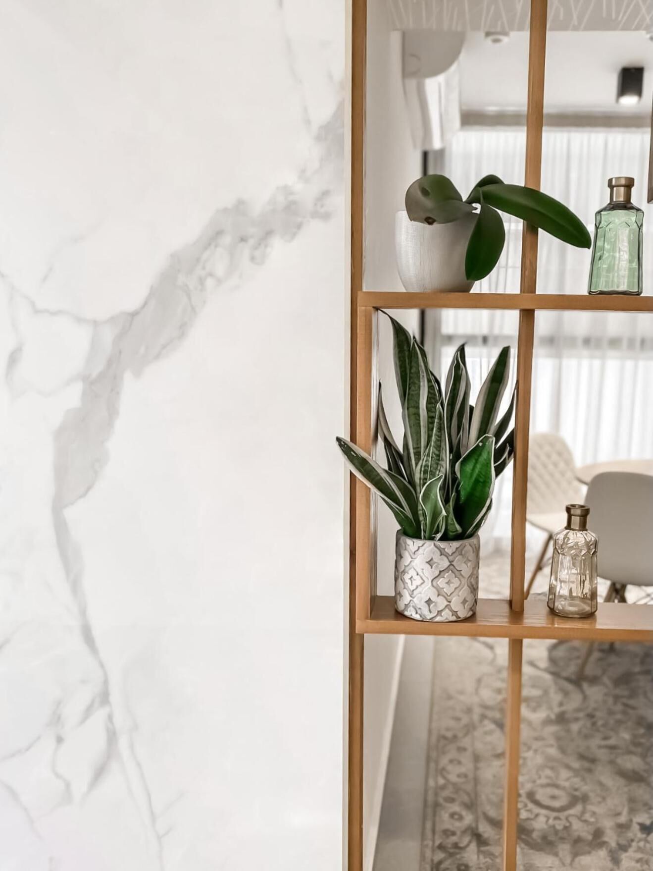 A marble wall with a wooden shelf holding a potted plant, a glass bottle, and a decorative item.
