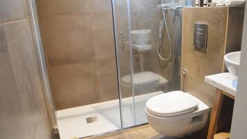 Un baño moderno con ducha envuelta en vidrio, inodoro blanco y lavamanos con encimera de mármol.