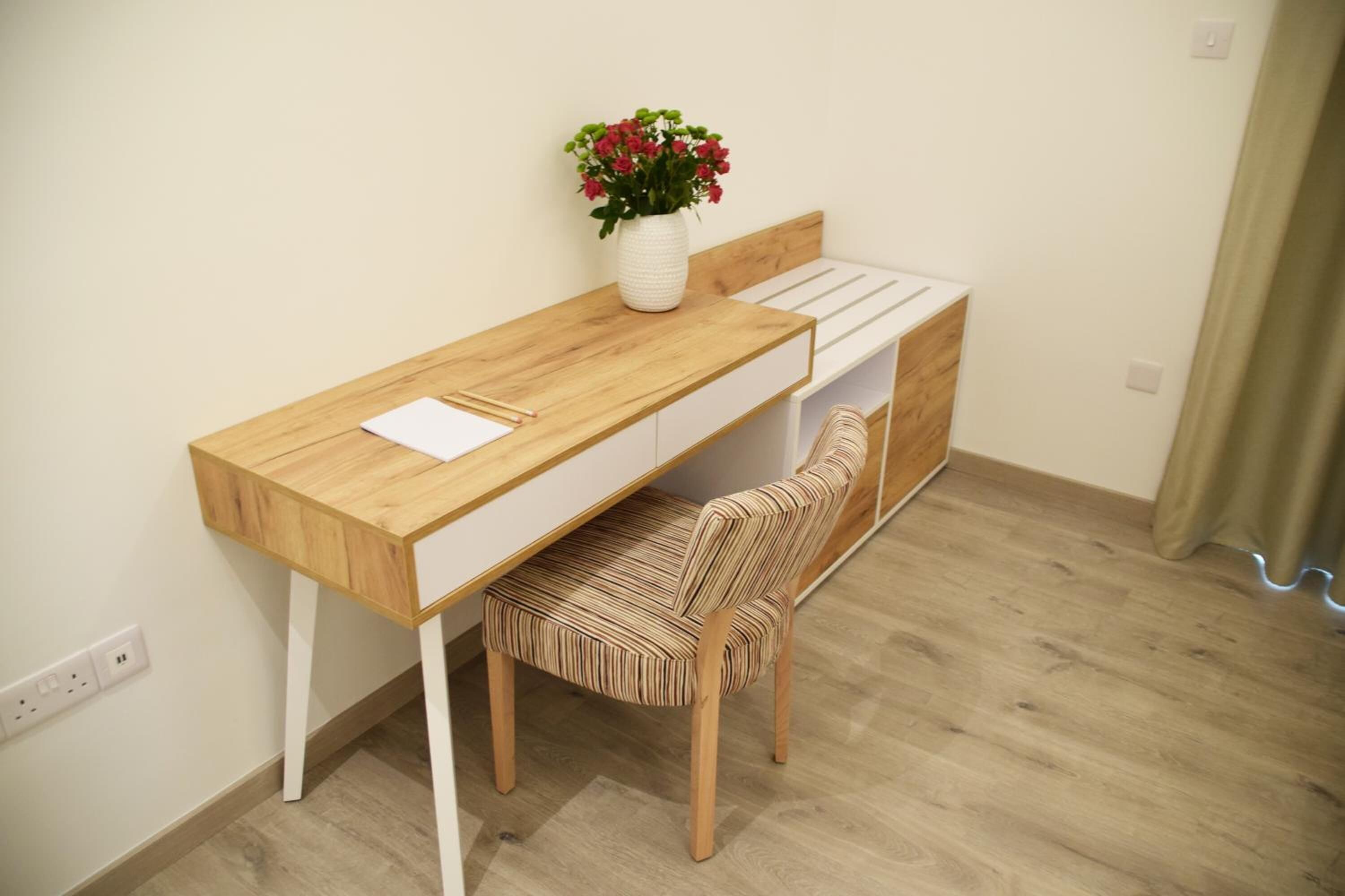 Un espacio de estudio pequeño con un escritorio de madera, una silla acolchada y un estante blanco.
