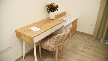Un espacio de estudio pequeño con un escritorio de madera, una silla acolchada y un estante blanco.