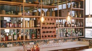 Zona de bar con estantes de botellas de licor, una cava de vinos y una barra con vasos y un frutero.