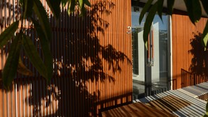 Un interior moderno con listones verticales de madera, un ventanal de vidrio que da a un balcón y un banco de madera.