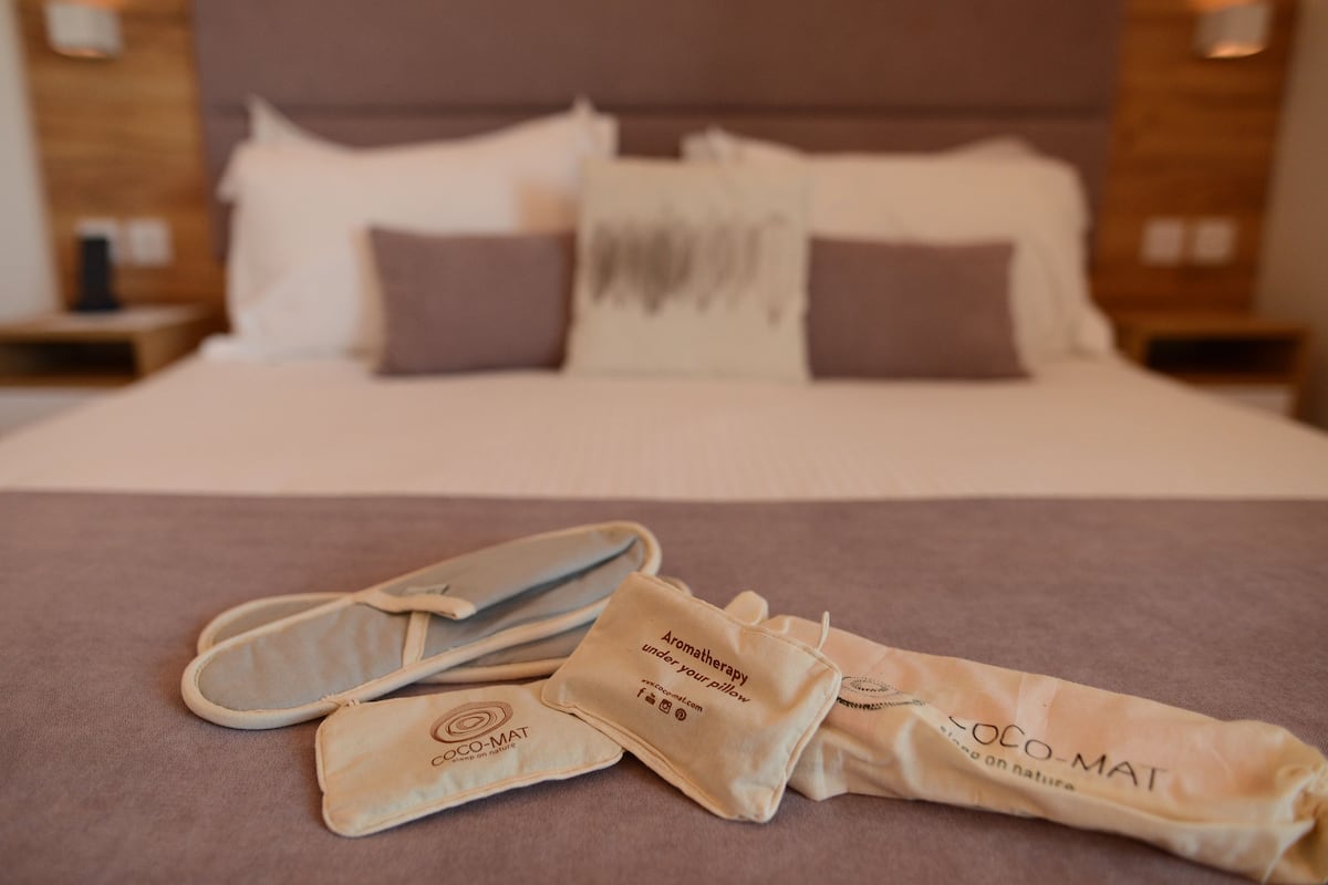 Een opgemaakt bed met kussens en een deken, een paar slippers en een handdoek met tekst erop.
