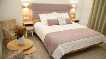 Une chambre d’hôtel moderne avec un grand lit, une table de chevet en bois, une petite table ronde en bois, une chaise et une petite table sur laquelle est posé un vase de fleurs.