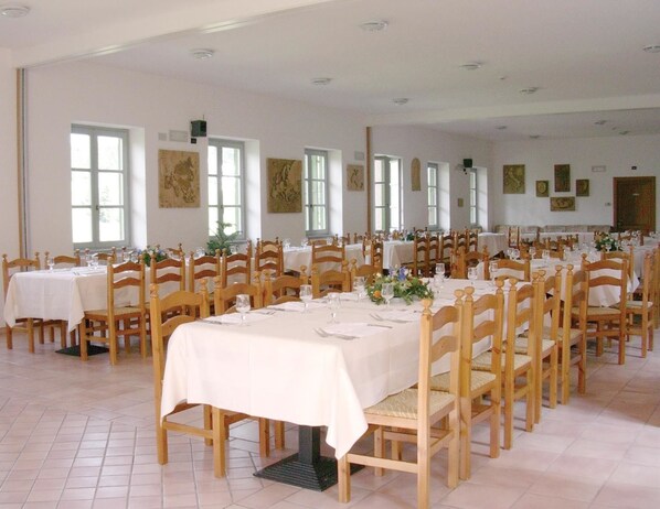 A large dining hall with multiple tables and chairs, arranged in rows.