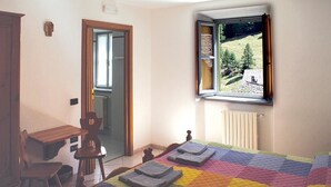 Une chambre à coucher comprenant un lit, un bureau, une chaise et une fenêtre donnant sur une maison et des arbres.