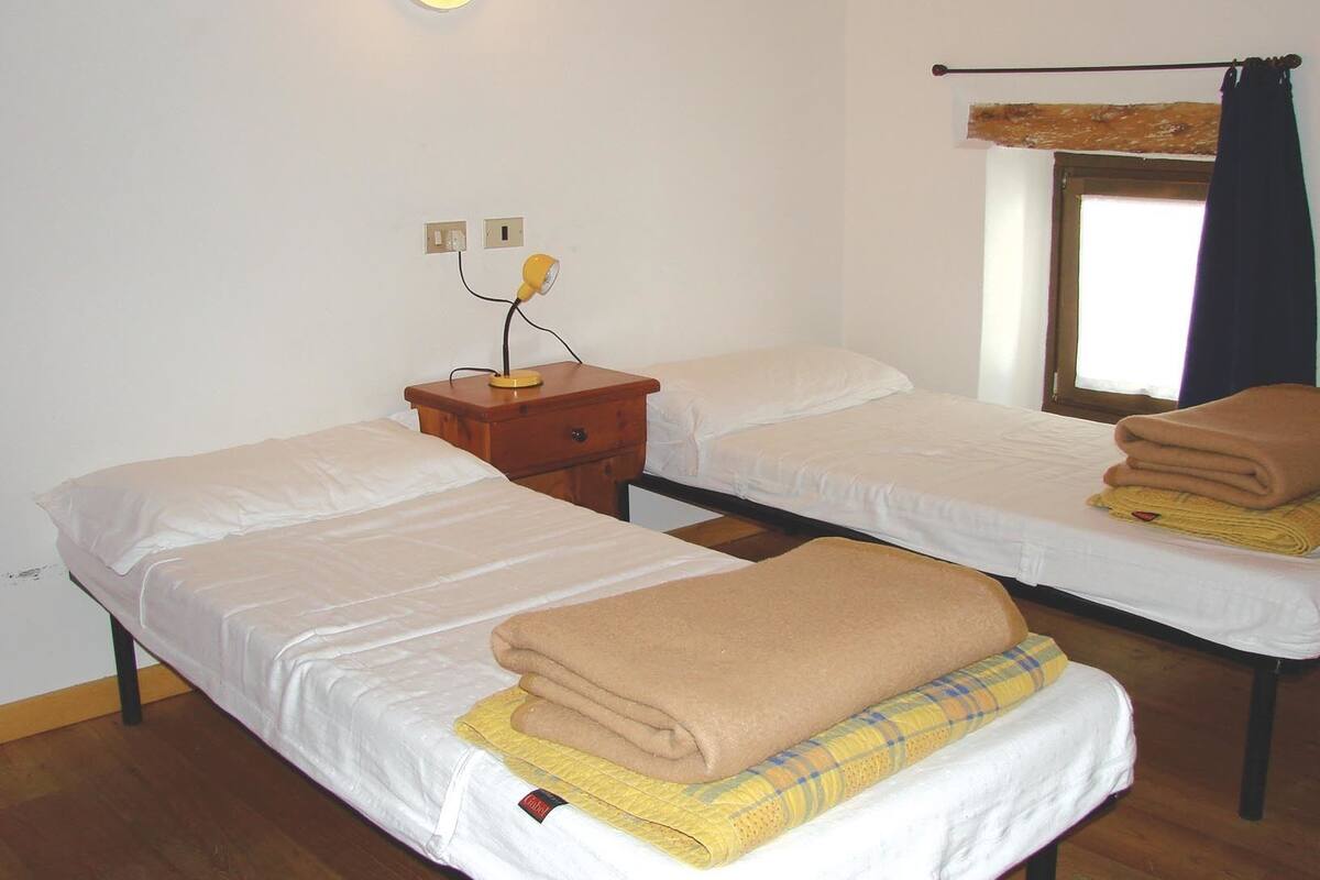 Une chambre avec deux lits simples, une table de chevet en bois avec une lampe, une fenêtre avec un rideau et un luminaire fixé au mur.