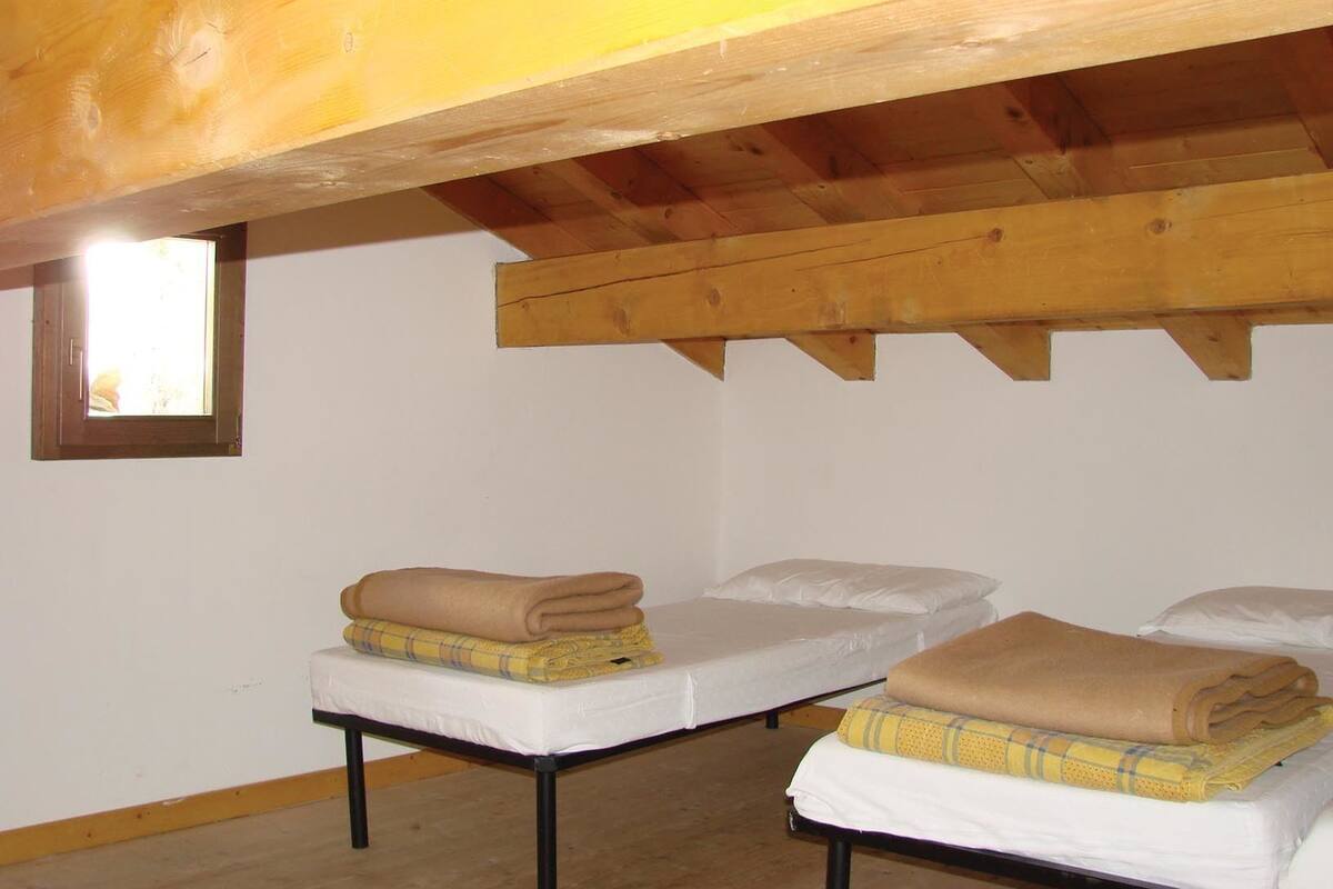 Une chambre avec deux lits, des poutres en bois, une petite fenêtre et un mur blanc.