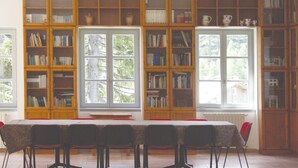 Une bibliothèque dotée de nombreuses étagères en bois, d’une grande table entourée de chaises et de grandes fenêtres donnant sur un paysage arboré.