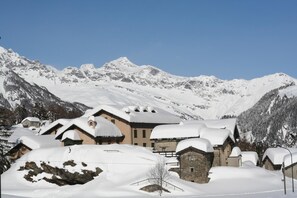 A snow-covered mountain village with traditional chalet-style buildings, a clear blue sky, and a backdrop of snow-capped peaks.