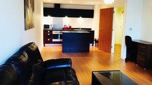 A modern living room with a black leather sofa, a glass coffee table, and a kitchen area with a central island, a microwave, and a stove. - Birmingham Serviced Apartment- Ryland (Birmingham)