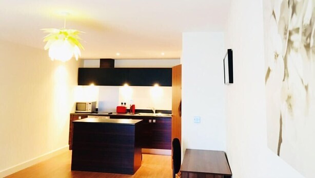 A modern kitchen with a central island, a dining area, and a large abstract painting on the wall. - Birmingham Serviced Apartment- Ryland (Birmingham)
