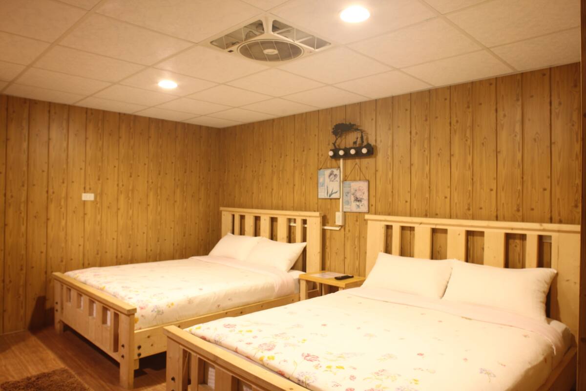 Une chambre avec deux lits en bois, une petite table de chevet et une étagère murale ornée de tableaux.