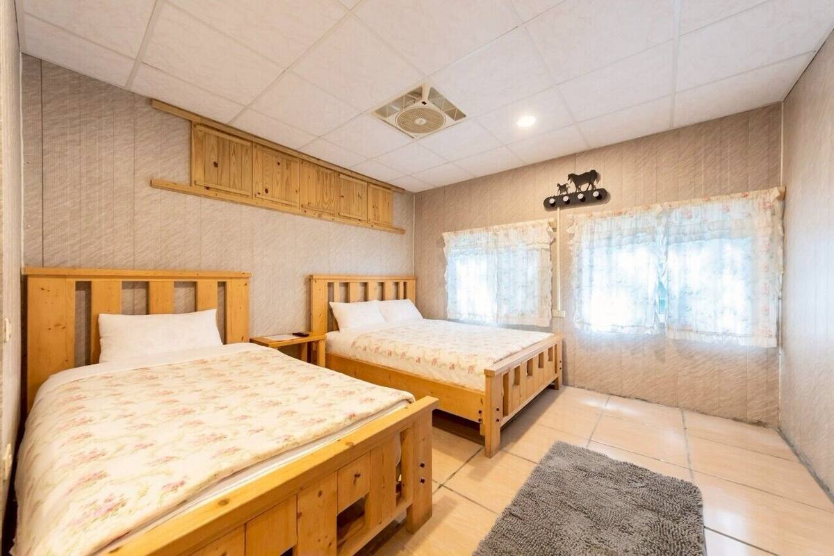 Une chambre avec deux lits en bois, un ventilateur de plafond et une fenêtre avec des rideaux.