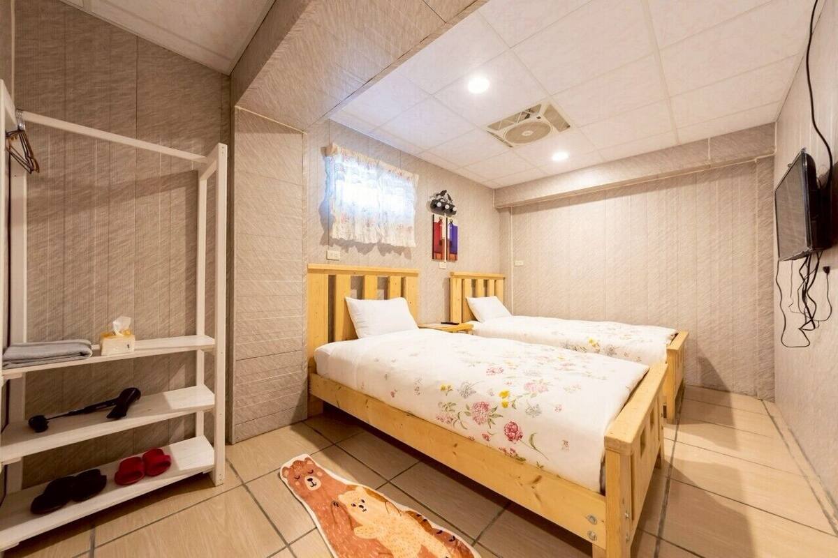 Une chambre avec deux lits, une étagère à chaussures, un tapis en forme d’ours en peluche et un téléviseur fixé au mur.