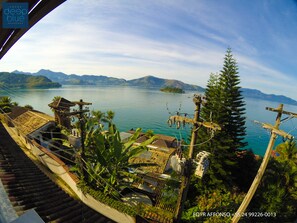 Vista costera con una casa tradicional, una pequeña isla y montañas al fondo.