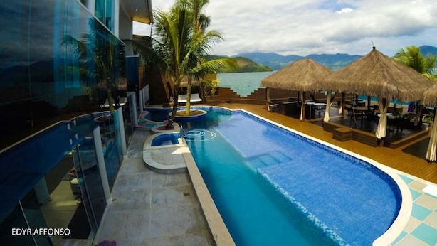 A modern hotel with a pool, palm trees, and a view of the sea. - Residência Angra Deep Blue (Angra dos Reis)