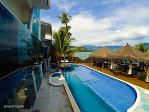 A modern hotel with a pool, palm trees, and a view of the sea. - Residência Angra Deep Blue (Angra dos Reis)