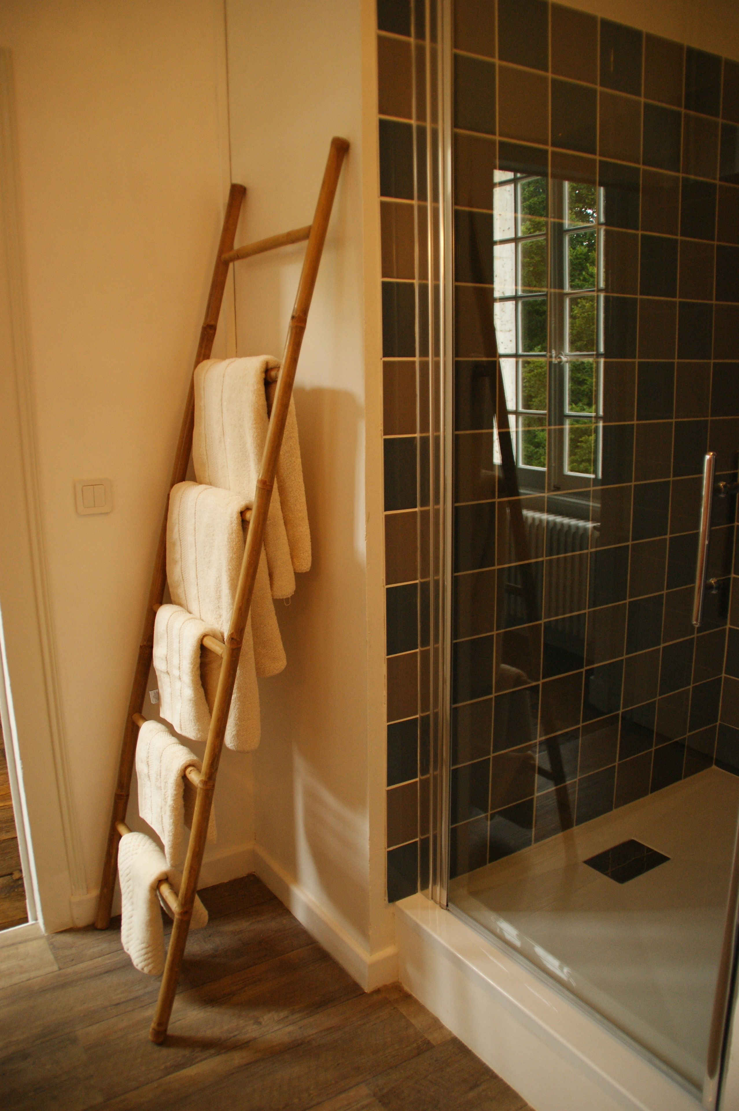 A shower area with a glass door, a wooden towel rack with towels, and a view of the outdoors through the window.