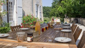 Een terras met houten tafels en stoelen, omgeven door een tuin met bloemen en een stenen muur.