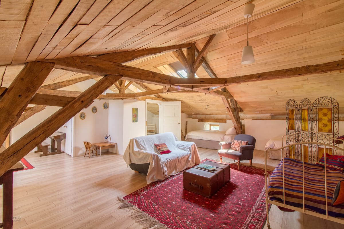 Un amplio dormitorio tipo loft con techo de madera alto, una cama acogedora, una mesita y una silla.