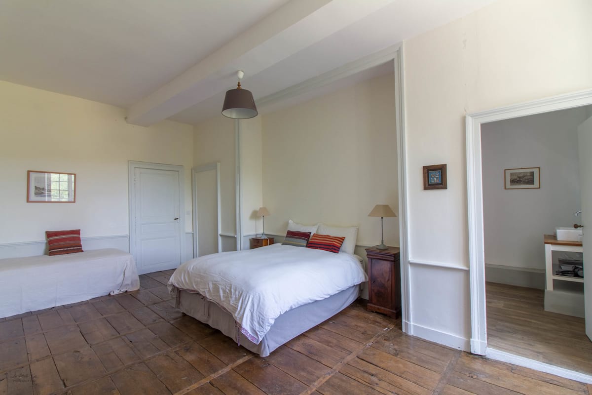 Un dormitorio con una cama grande, dos mesitas de noche, un armario y una puerta que da a otra habitación.
