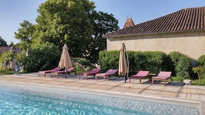 A poolside area with lounge chairs and umbrellas, a clear pool, and a building with a tiled roof. - Château de La Combe (Mareuil en Périgord)