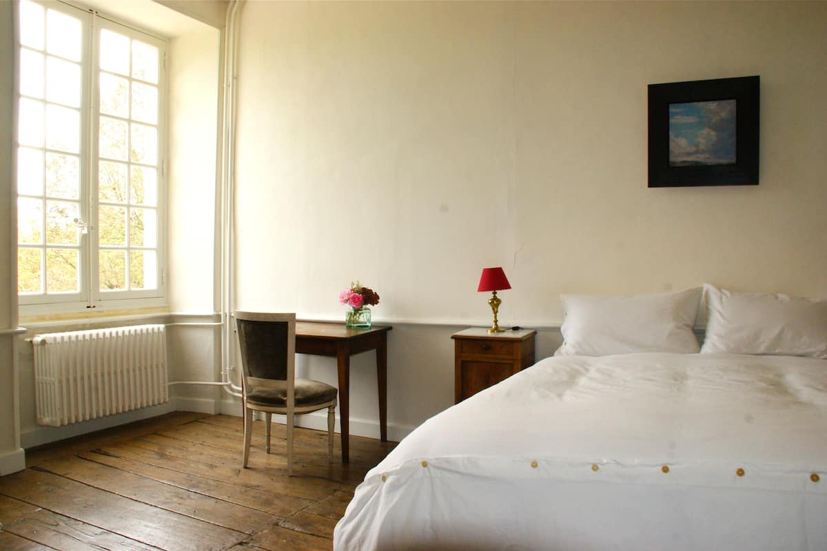 Un dormitorio con suelo de madera, una cama, un escritorio con silla, un radiador y una ventana.