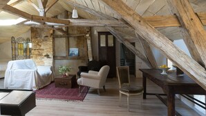Een knus zolderkamertje met zichtbare houten balken, een bed, een stoel, een klein tafeltje en een potplant.