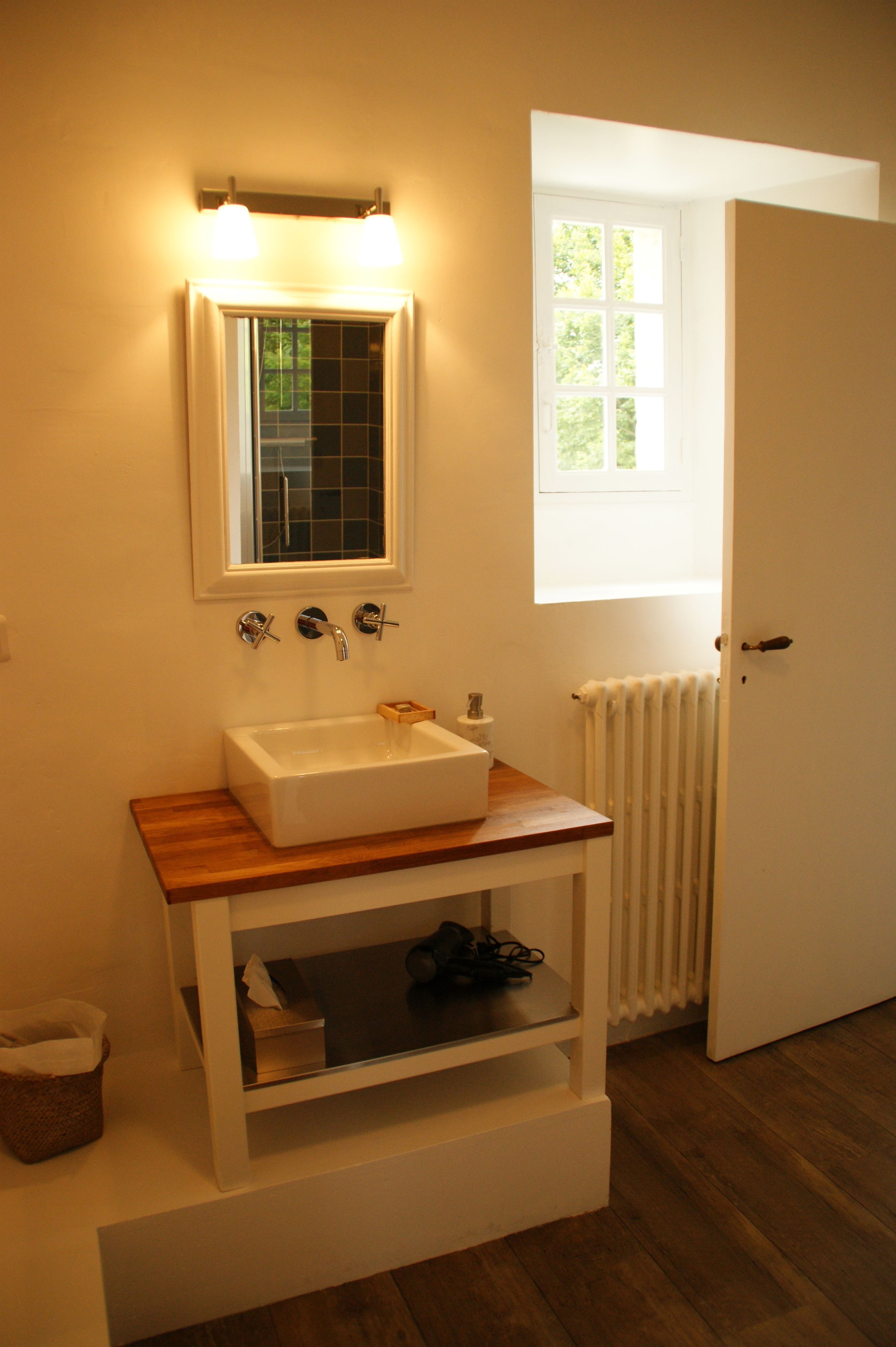 A bathroom with a white sink, wooden countertop, and a mirror above it. There is a window with a view of greenery outside.