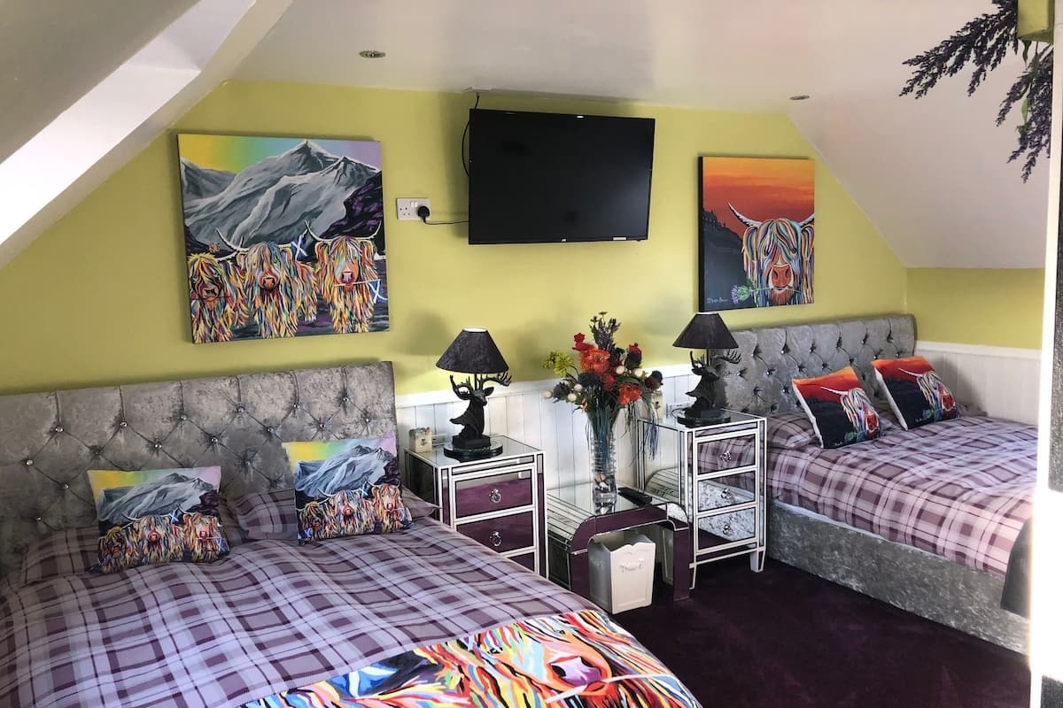 A bedroom with two beds, a TV, and artwork on the walls.