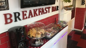 A breakfast bar with a TV mounted above it, a coffee machine, and a fruit display. - Gleninver Guest House (Inverness)